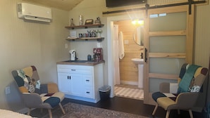 Een kleine leefruimte met een kitchenette, twee stoelen, een bed en een schuifdeur naar een badkamer.
