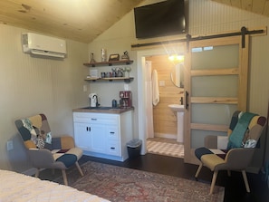 Een kleine leefruimte met een kitchenette, twee stoelen, een bed en een schuifdeur naar een badkamer.