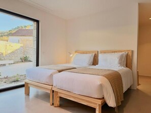 Ein Schlafzimmer mit zwei Betten, einem großen Fenster und Blick ins Freie.