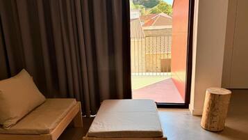 Une pièce comprenant un banc en bois, un petit tabouret et une fenêtre donnant sur un espace extérieur délimité par une clôture en bois.