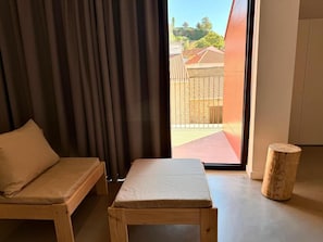 Una habitación con un banco de madera, un taburete pequeño y vistas a un espacio exterior con valla de madera.
