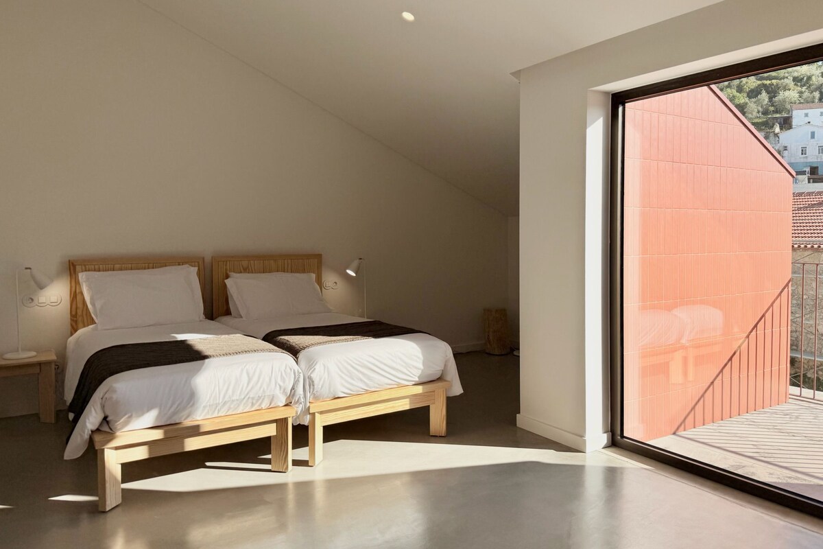 Ein Schlafzimmer mit zwei Betten, einem großen Fenster und Blick ins Freie.