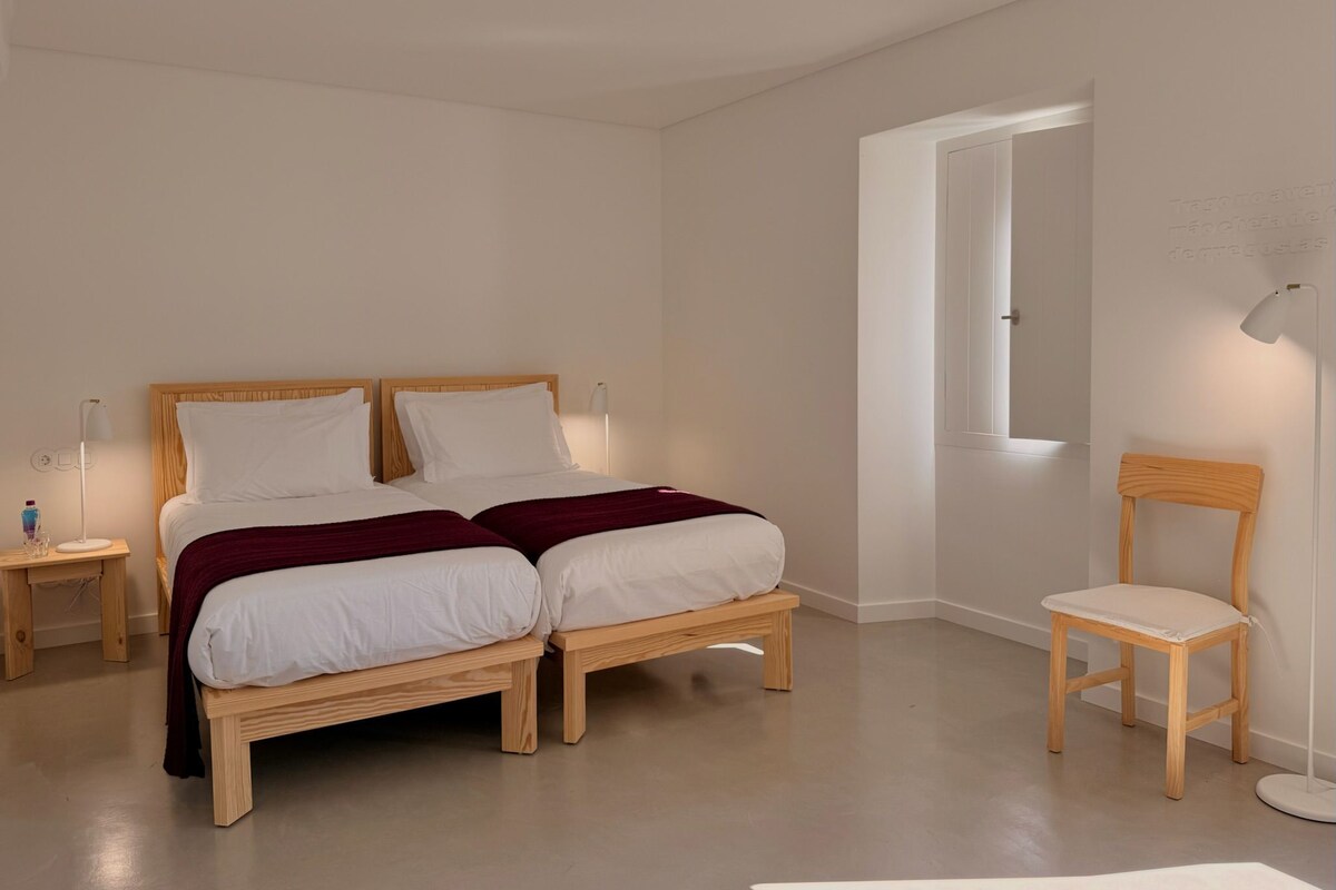 Ein schlicht eingerichtetes Schlafzimmer mit Doppelbett, Nachttischen, einem Sessel und einer Stehlampe.