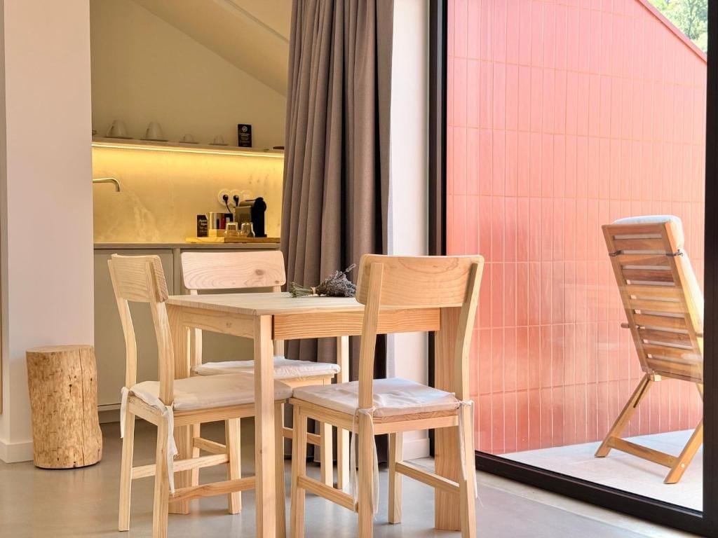 Un comedor con una mesa y sillas de madera, un taburete pequeño y un ventanal con cortinas.
