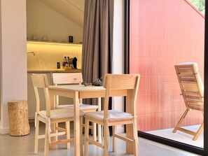 Ein Essbereich mit einem Holztisch und Stühlen, einem kleinen Hocker und einem Fenster mit Vorhängen.