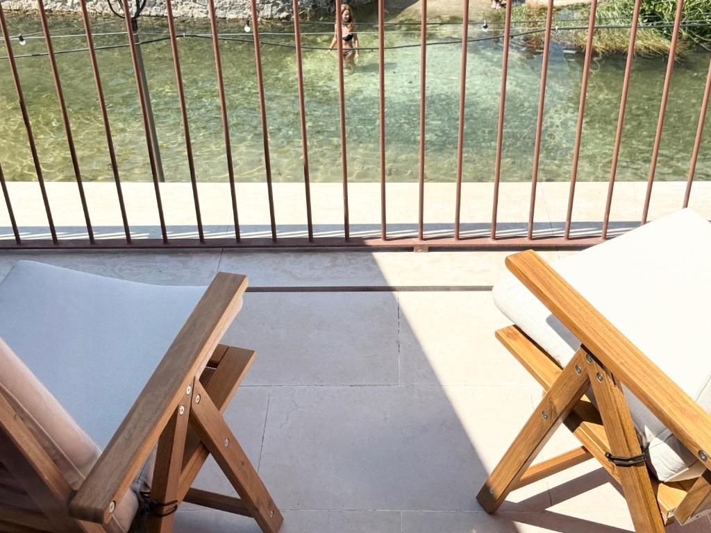 A balcony with a view of a body of water, two wooden lounge chairs, and a metal railing.