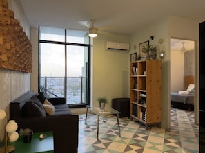 A modern living room with a sofa, a glass coffee table, a bookshelf, and a large window offering a city view. - Moderno dpto. con Vistas y Terraza (Monterrey)