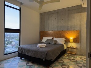 Une chambre à coucher avec un lit, une table de chevet, une lampe et une vue sur la ville par la fenêtre.