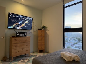 A bedroom with a bed, a television mounted on the wall, a dresser, and a window with a city view. - Moderno dpto. con Vistas y Terraza (Monterrey)