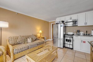 A compact living space with a sofa, a coffee table, a refrigerator, an oven, and a microwave. - Oceanfront Resort Condo - Beach + Pool Views (Daytona Beach)