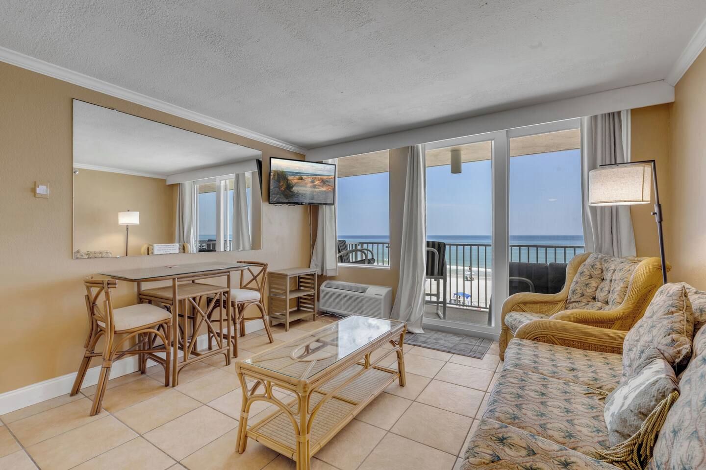 A hotel room with a balcony, a dining area, a sofa, and a TV.
