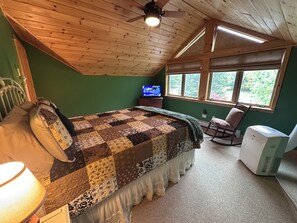 A bedroom with a wooden ceiling, a quilted bedspread, a television, and a rocking chair. - Valeside Lodge: Whiteface views, firepit, privacy, woodstove, rec room (Jay)