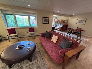 A living room with a red sofa, two armchairs, a wooden bench, a coffee table, and a bunk bed in the background. - Valeside Lodge: Whiteface views, firepit, privacy, woodstove, rec room (Jay)
