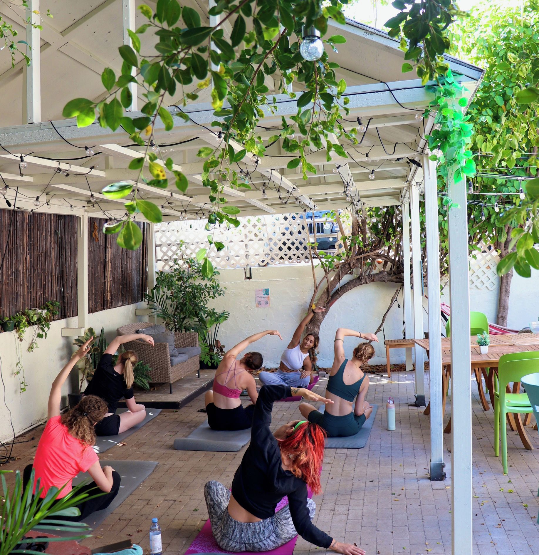 Un cours de yoga en plein air, où les participants pratiquent sur des tapis placés sous une pergola illuminée de guirlandes lumineuses.