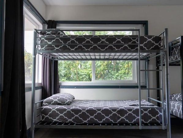 Una cama litera con ropa de cama estampada, una ventana con cortinas y vistas al exterior con vegetación.