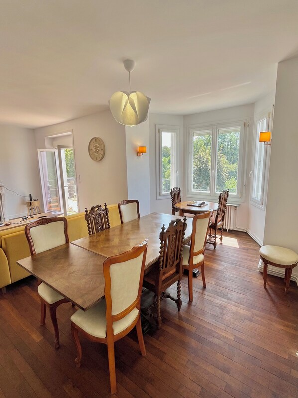 A dining area with a wooden table and chairs, a chandelier, and large windows with a view of trees. - Ti Ar Meliner – In the Heart of Brittany’s Natural Beauty (langonnet)