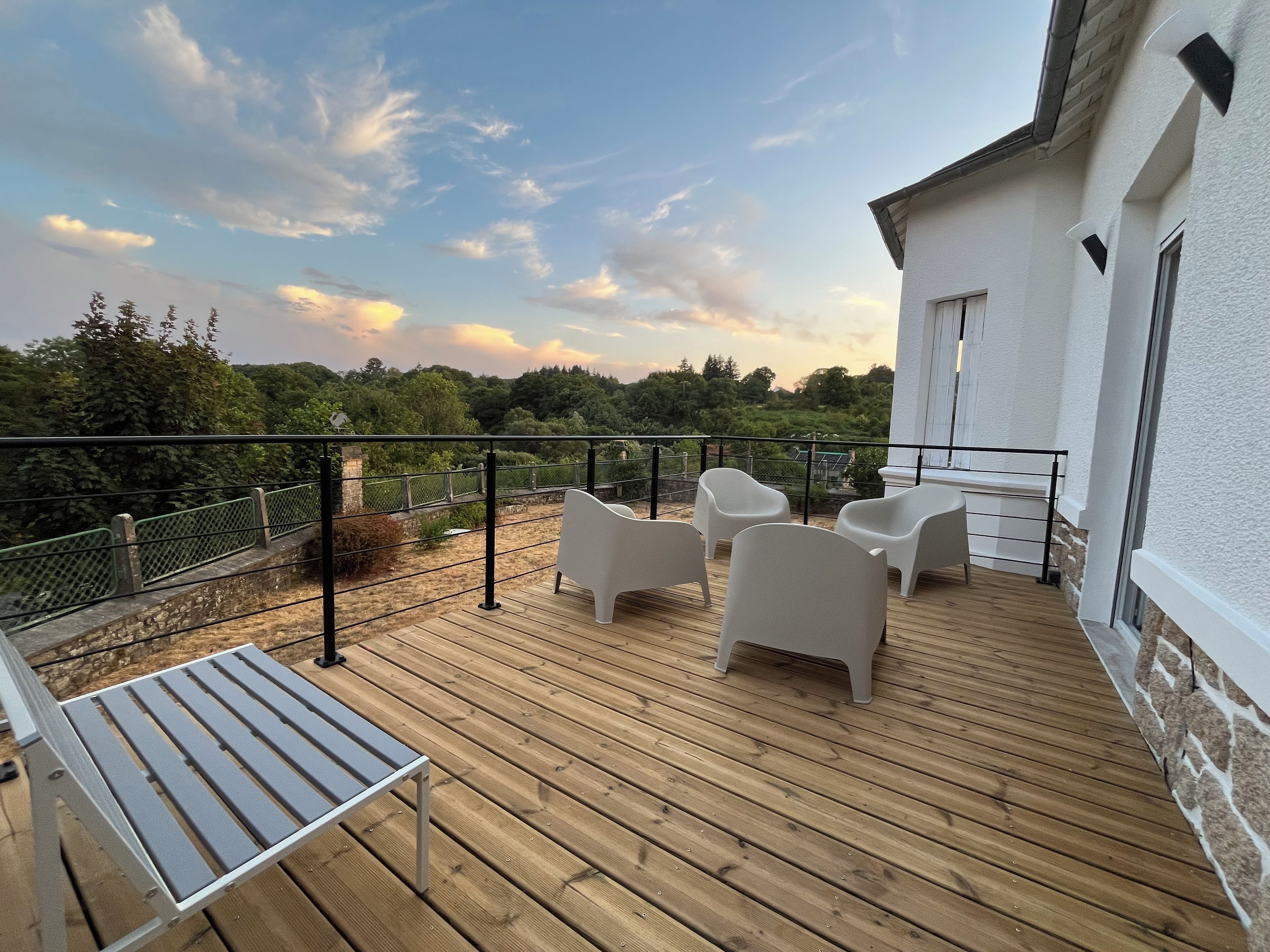 A wooden deck with outdoor furniture, a white building, and a view of greenery.