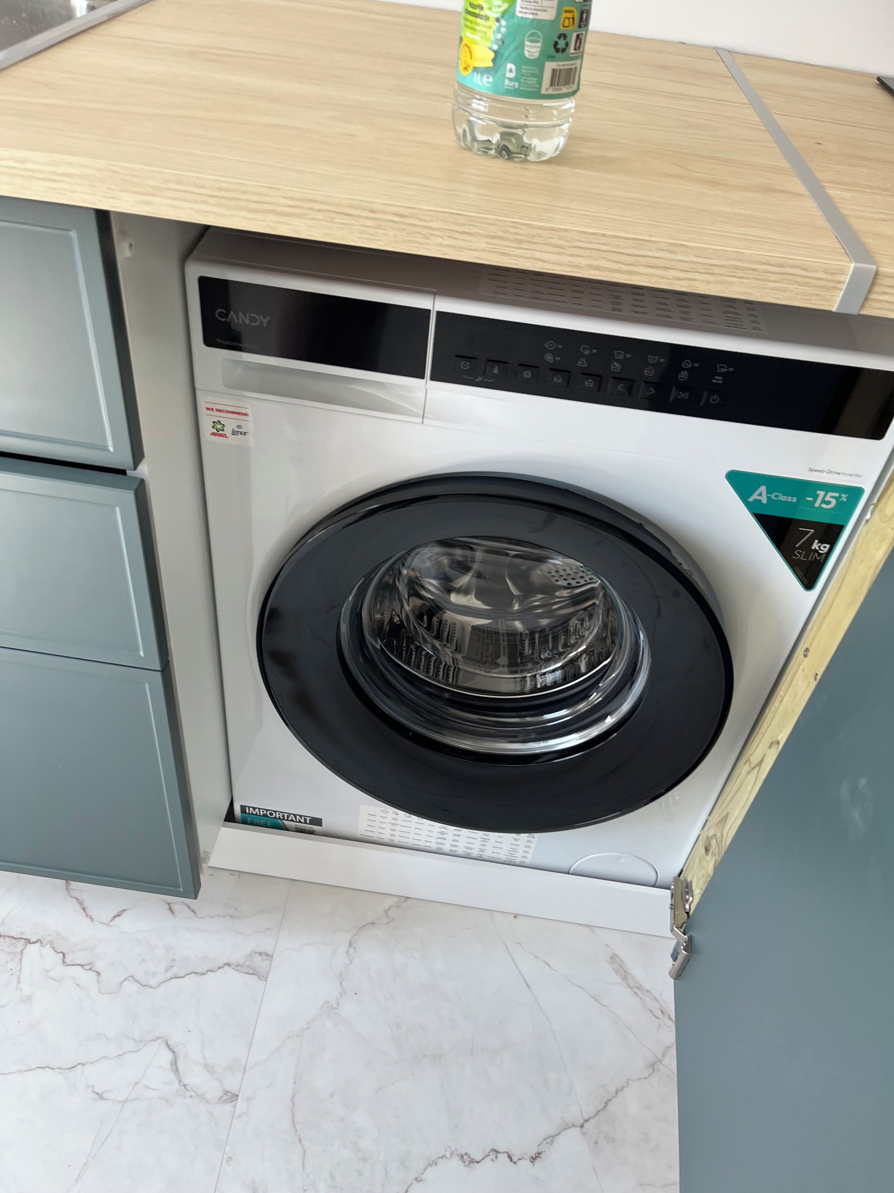 Un lave-linge compact et moderne, doté d’un panneau de commande, installé dans un petit espace buanderie avec un sol en marbre.