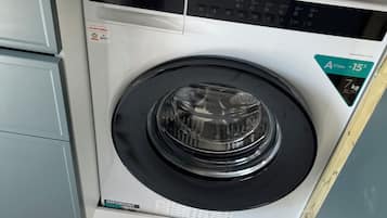 Un lave-linge compact et moderne, doté d’un panneau de commande, installé dans un petit espace buanderie avec un sol en marbre.