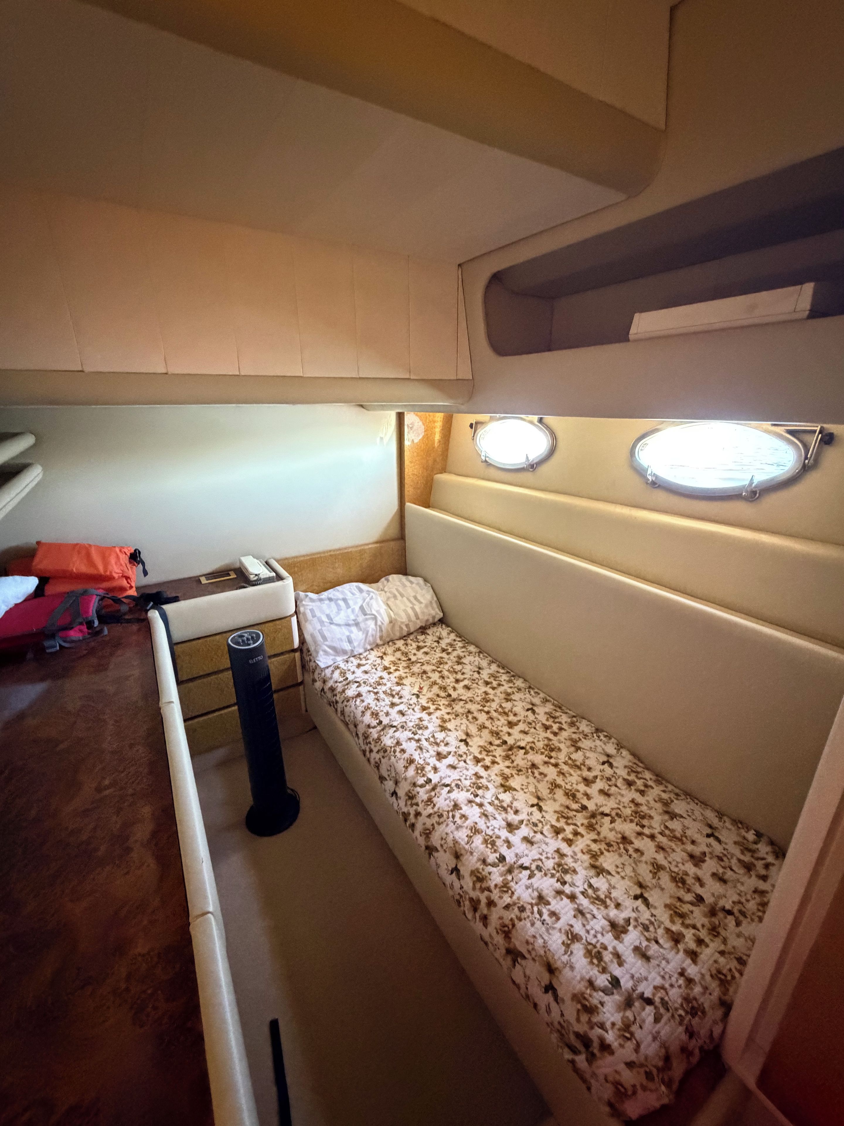 Quarto compacto com cama, uma mesinha e janela com luminária.