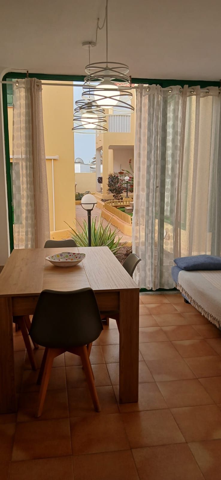 Comedor con una mesa y sillas de madera, un tazón y vistas a un patio exterior con plantas y una lámpara.