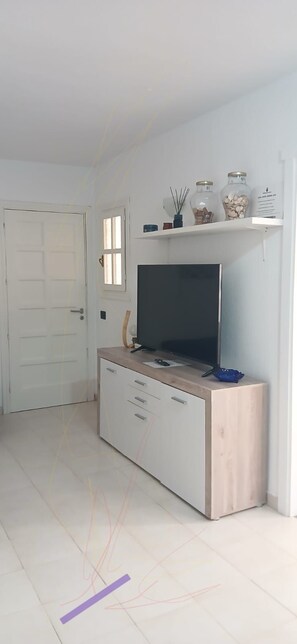 A room with a television on a wooden cabinet, a white door, and a window. - CABO PARAISO (Costa de Antigua)