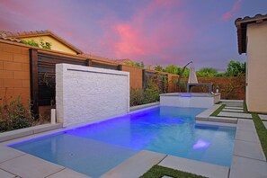 A swimming pool with a white wall and a blue-lit edge, surrounded by a brick wall and a wooden fence. - La Quinta Oasis w/Pool, Hot Tub, Outdoor Kitchen, 4bedrooms/4baths (La Quinta)