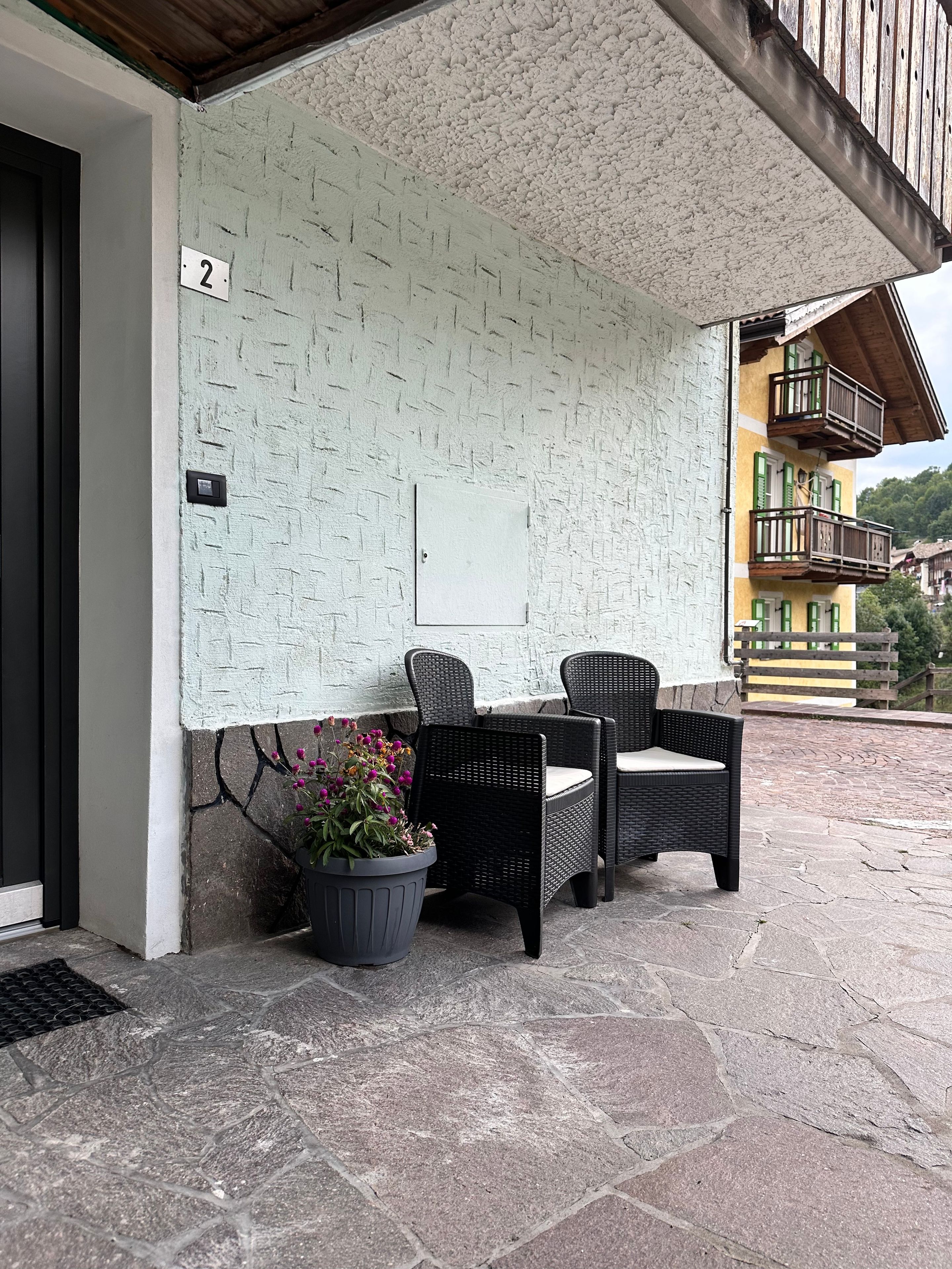 Ein Sitzbereich im Freien mit Korbmöbeln, einem Blumentopf und einer strukturierten Wand.