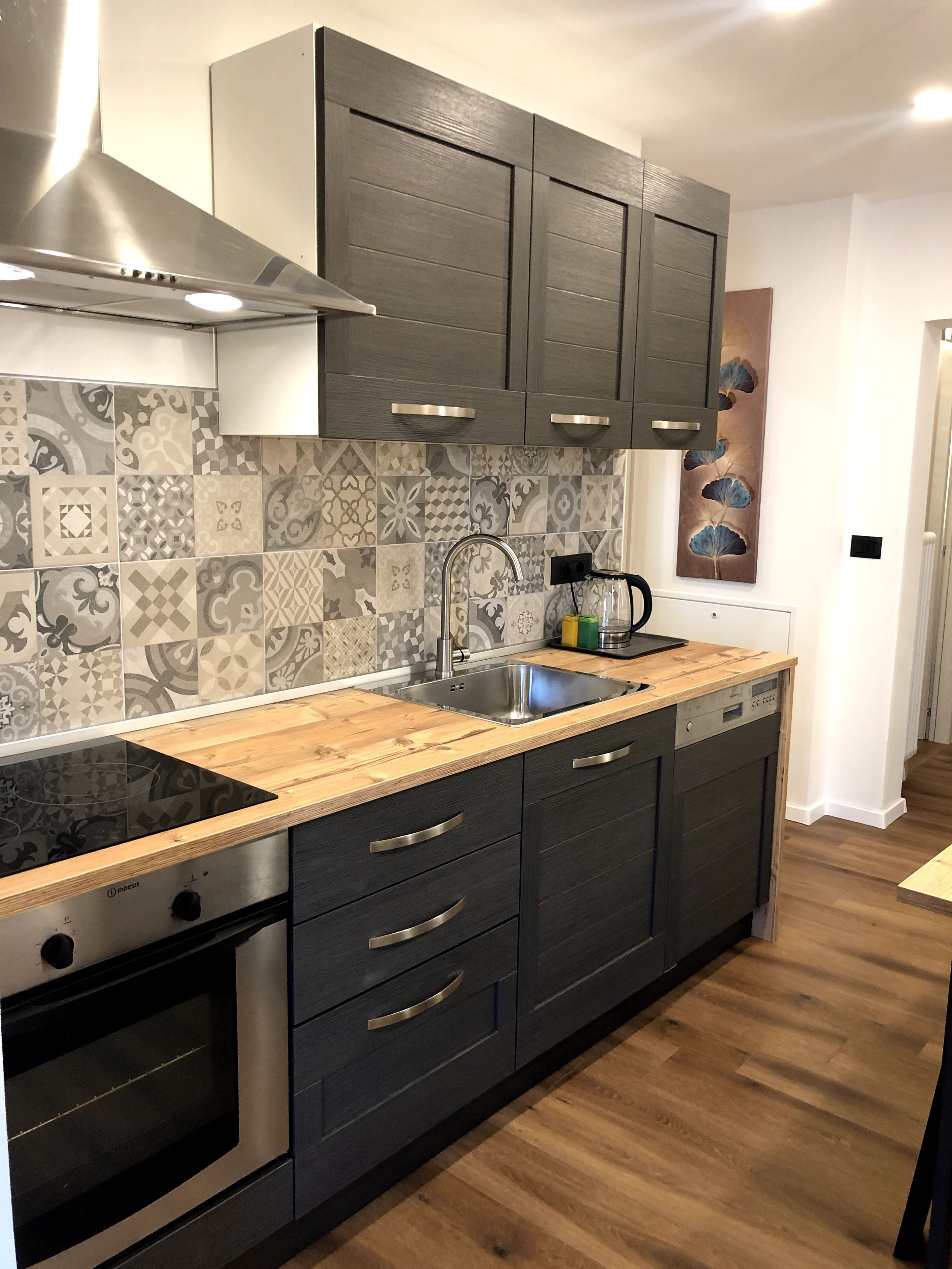 Une cuisine moderne avec des meubles de couleur sombre, un évier en acier inoxydable et un pare-feu décoratif.