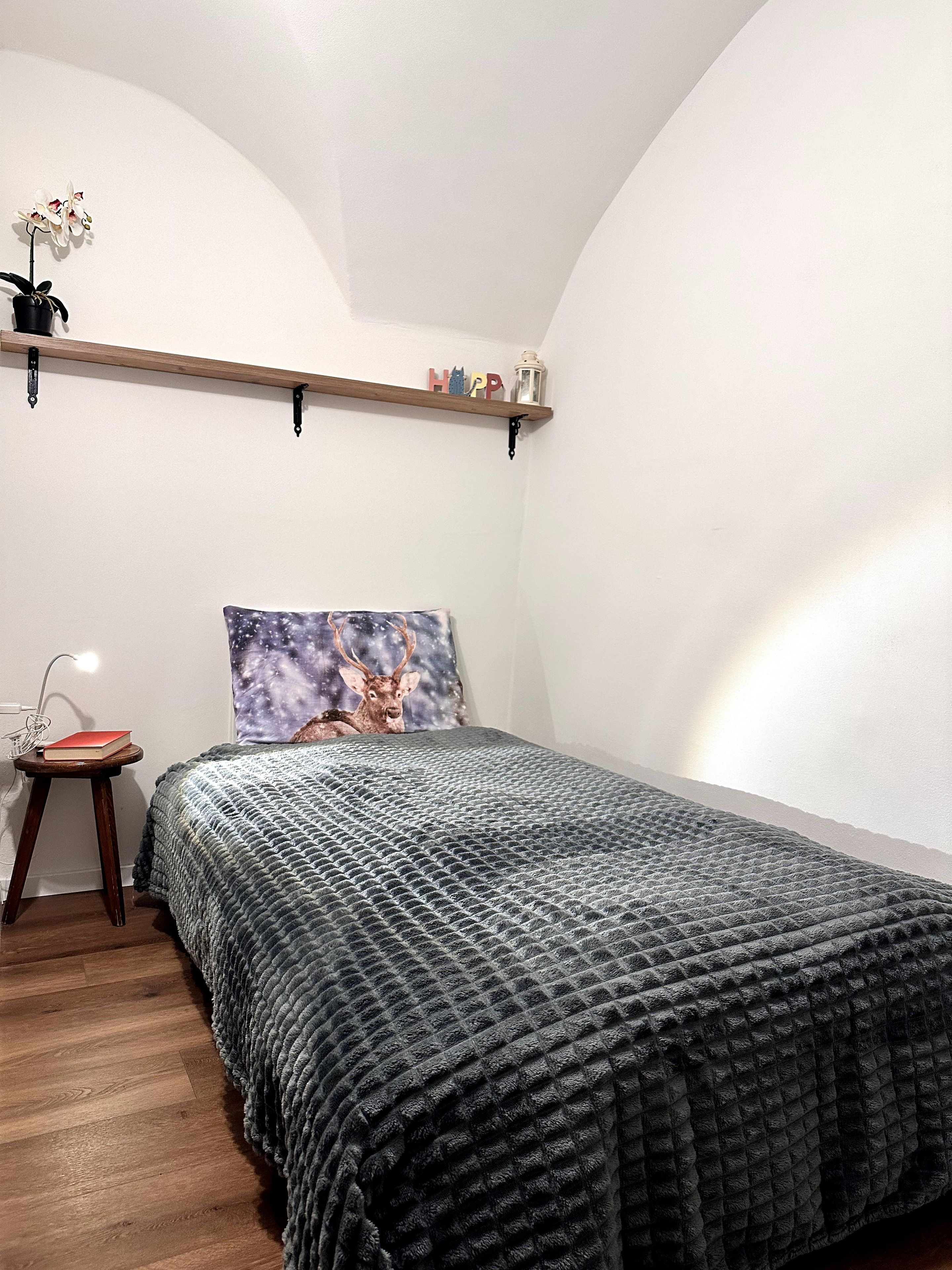 Een slaapkamer met een bed, een nachtkastje, een plank met decoratieve objecten en een muur met een schilderij.