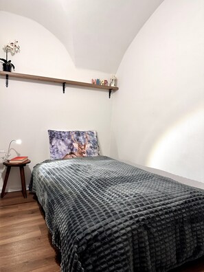 Un dormitorio con cama, mesita de noche, estante con objetos decorativos y un cuadro en la pared.