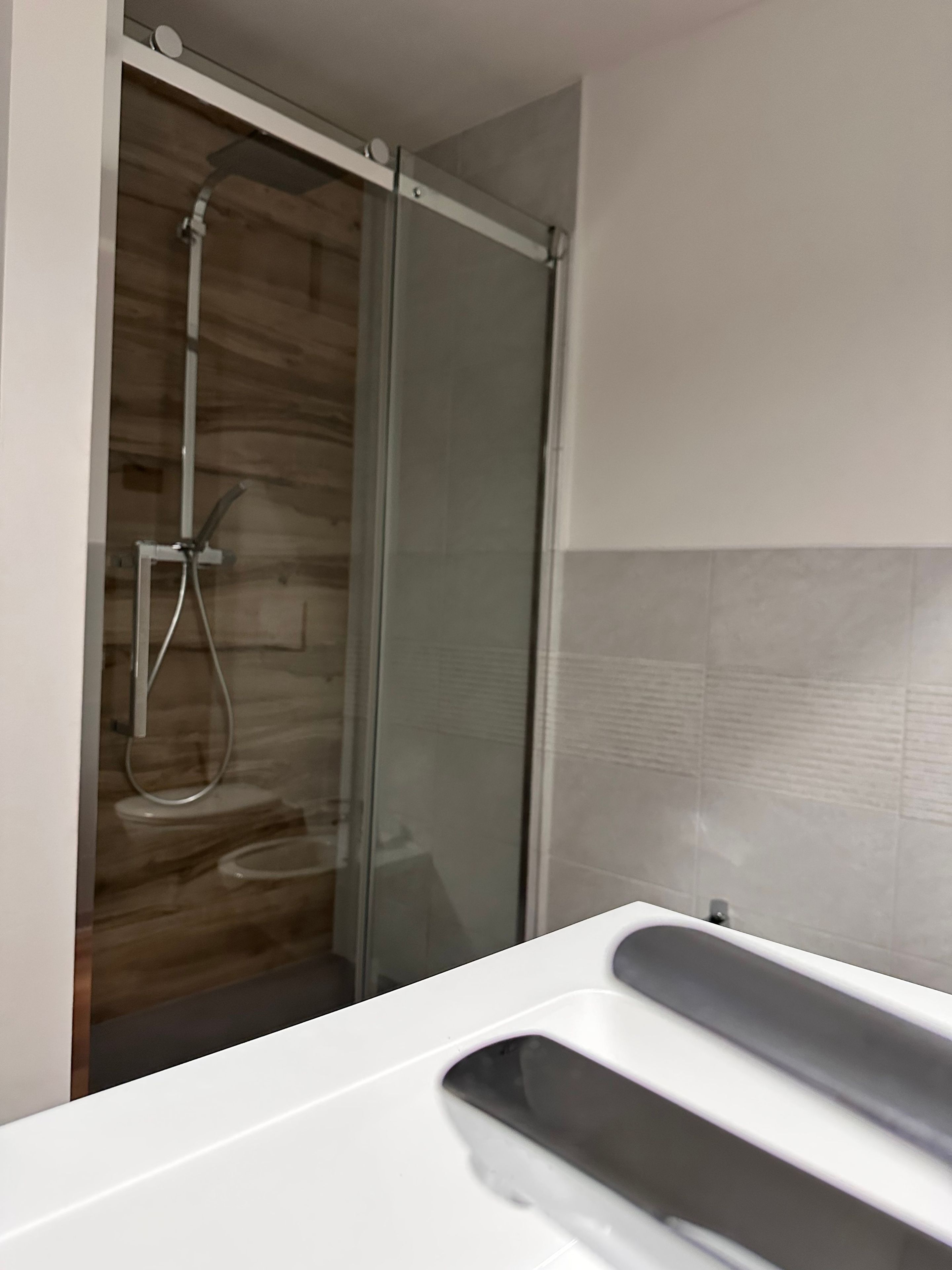 Une salle de bain moderne avec une douche à parois de verre, un lavabo blanc et un mur recouvert de carreaux.