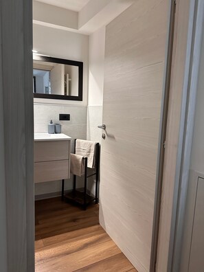 A bathroom with a wooden floor, a sink with a towel, and a mirror above the mirror.