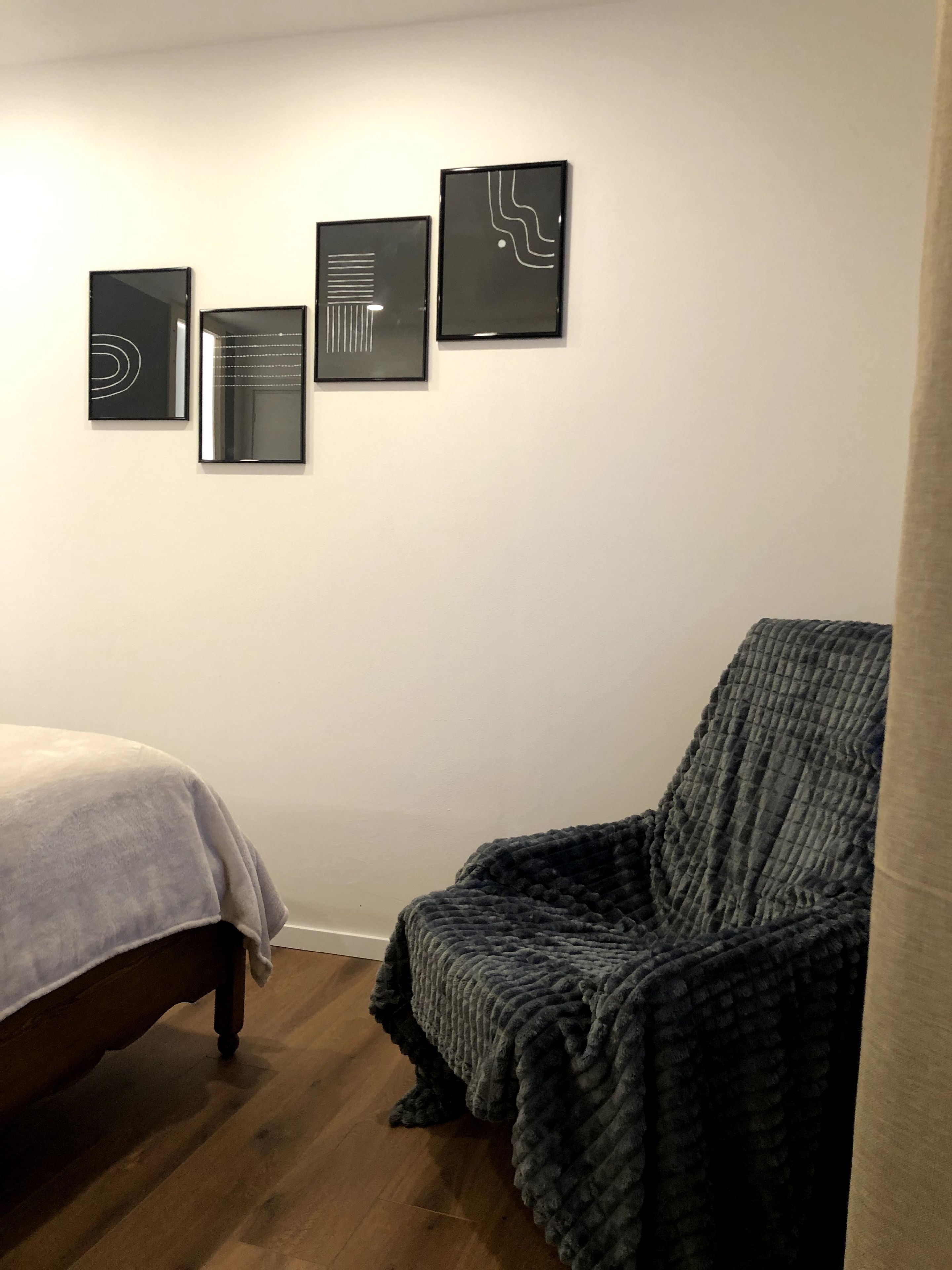 Un dormitorio con una cama, una silla y tres obras de arte enmarcadas en la pared.