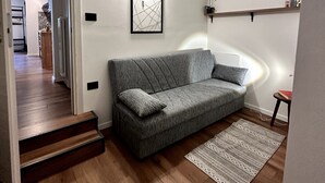 A modern living room with a grey sofa, a framed abstract artwork, a small table with a book, and a staircase leading to another room. - Vacation Home 'Ele Carano House' with Mountain View and Wi-Fi (Carano)