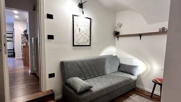 Una sala moderna con un sofá gris, una obra de arte abstracta enmarcada, una mesita con un libro y una escalera que lleva a otra habitación.
