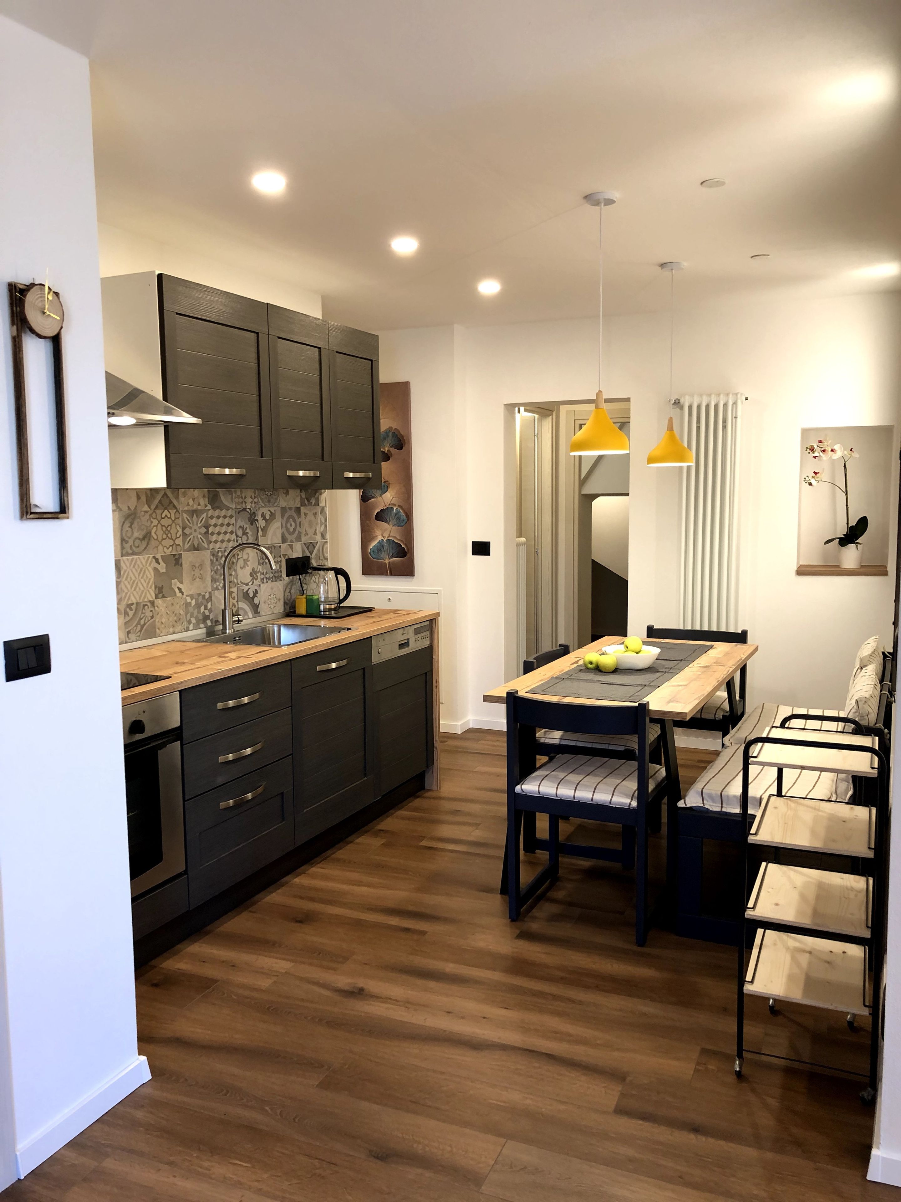 Una cocina moderna con armarios oscuros, encimera de madera y comedor con mesa y sillas.
