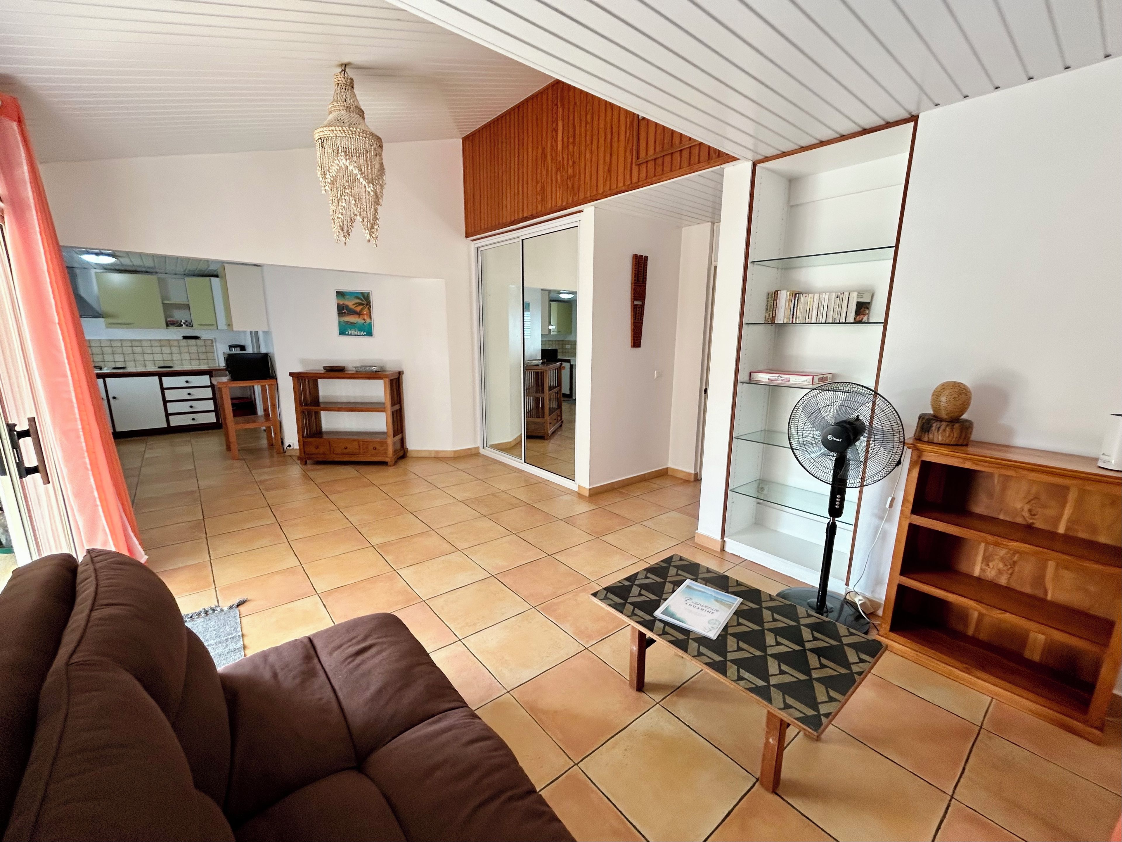 Een woonkamer met een bank, een bijzettafeltje, een ventilator en een houten kast.