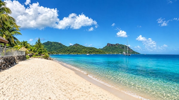 A beach with clear turquoise water, a sandy shore, and a mountain in the background.