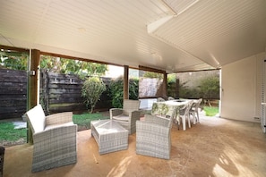 An outdoor patio area with wicker furniture and a table, surrounded by a wooden fence and greenery.