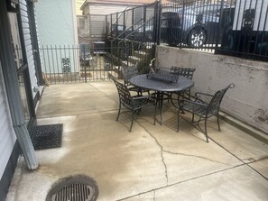 A patio with a round metal table and chairs, a metal fence, and a parked car in the background. - Little Italy 1BR Apartment just off Taylor Street (Chicago)