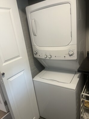 A front-loading washer and dryer unit with control knobs and buttons, positioned against a wall with a door to the left. - Little Italy 1BR Apartment just off Taylor Street (Chicago)