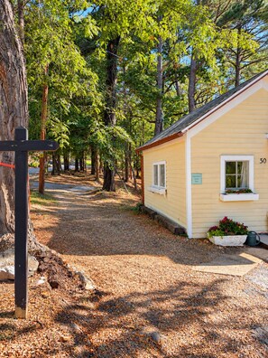 A small yellow building with a number '30' on the side, surrounded by trees and a gravel path. - Crown & Cedar Cozy Uptown Pets OK Deluxe Qn Bed EV Charger (Eureka Springs)