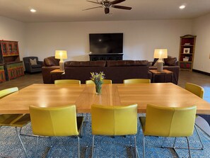 A dining area with a wooden table and yellow chairs, a brown sofa set, a flat-screen TV mounted on the wall, and a patterned carpet. - Large Modern Mountain Lodge in Forest near Lake Mary - Sleeps 12 - Pets OK (Flagstaff)