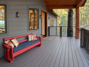 A wooden deck with a red bench and a door leading to a covered area. - Large Modern Mountain Lodge in Forest near Lake Mary - Sleeps 12 - Pets OK (Flagstaff)