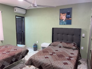 A room with two beds, a ceiling fan, an air conditioning unit, a trash bin, and a painting on the wall. - Casa del Sol Colima (Colima)
