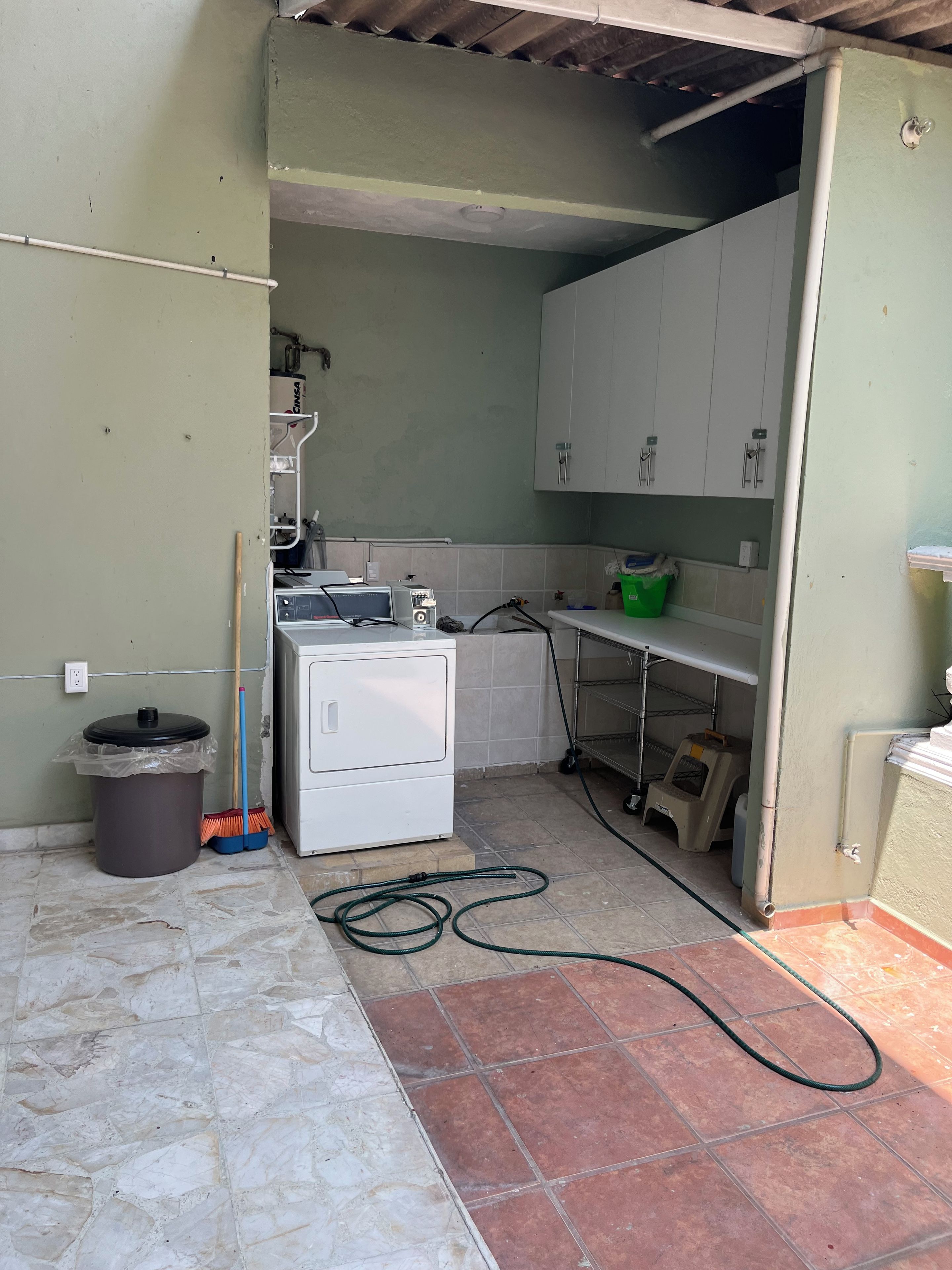 Une petite cuisine équipée d’un lave-linge, d’une poubelle et d’un balai.