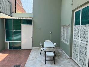 Un petit espace patio avec une table et des chaises, une porte et une fenêtre munie d’un grillage métallique.