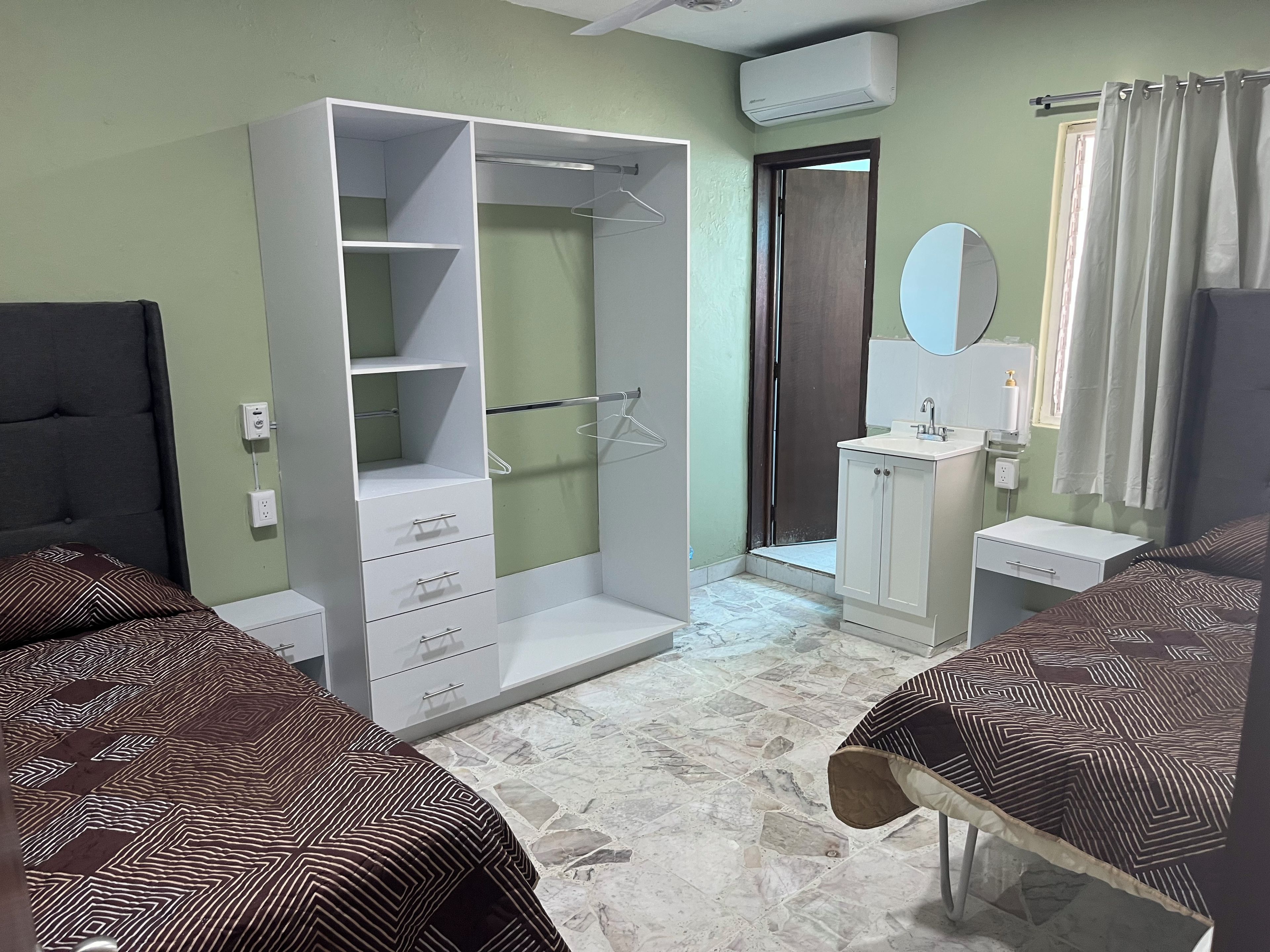 A bedroom with a wardrobe, a bed, a bathroom with a sink and mirror, and a shower area.
