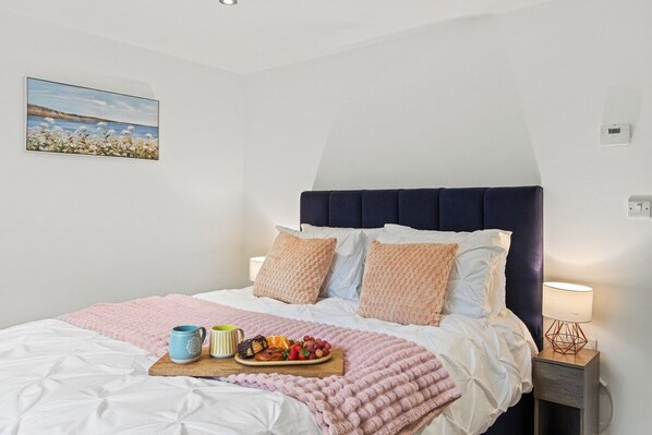 Ein ordentlich bezogenes Bett mit einer rosa Decke, eine Platte mit Obst und Gebäck sowie zwei Tassen.